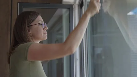 Woman is cleaning window from inside using a squeegee tool Stock Footage 315234650