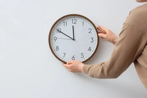 Woman with clock on light wall, back view. Daylight saving time concept Stock Photos