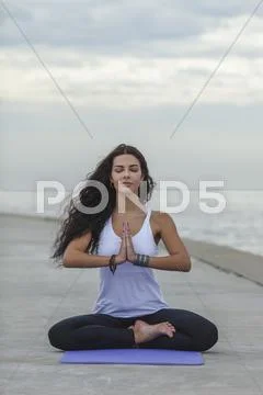Woman With Closed Eyes Practicing Yoga In Prayer Position At Beach Against