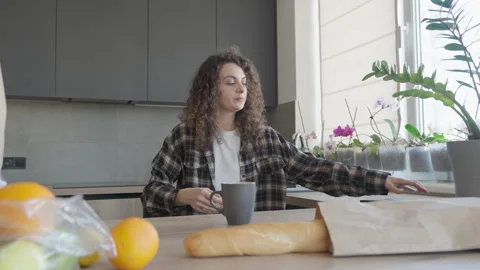 Woman Closing Tablet While Sitting In Kitchen With Mug, Fresh Groceries Nearby 스톡 동영상 306396350