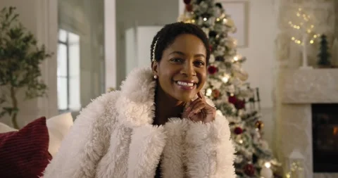 Woman in coat responding to camera on sofa, propping chin, turning, smiling by Stock Footage 344459488
