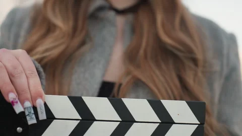 Woman in coat tapping clapper on vibrant city film shoot. Elegant woman in grey Stock Footage 342431713