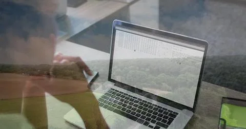 Woman coding on laptop and checking smartphone in home office with rural view, Stock-Fotos