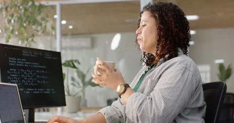Woman coding on screen at work desk while sipping mug, pausing and stretching Stock Footage 347823752