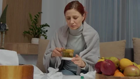 Woman with cold drinks herbal tea on couch while treating her symptoms Stock Footage 346706404