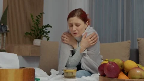 Woman with cold sits on couch drinking tea while resting and recovering at home Stock Footage 346706240