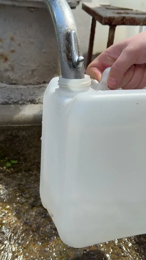 Woman collecting spring water into a plastic canister from an outdoor pipe in a Stock Footage 345183053