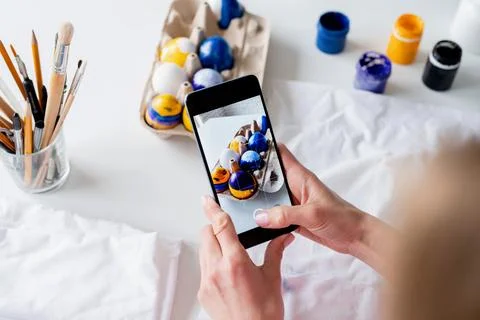 Woman coloring Easter eggs in the kitchen, taking photo on mobile Stockfoto's