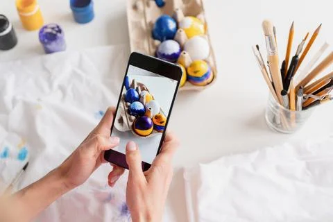 Woman coloring Easter eggs in the kitchen, taking photo on mobile Stockfoto's