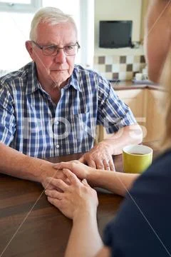 Woman Comforting Unhappy Senior Man Sitting In Kitchen At Home Stock Photos