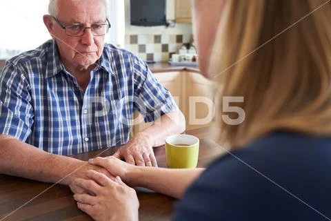 Woman Comforting Unhappy Senior Man Sitting In Kitchen At Home Stock Photos
