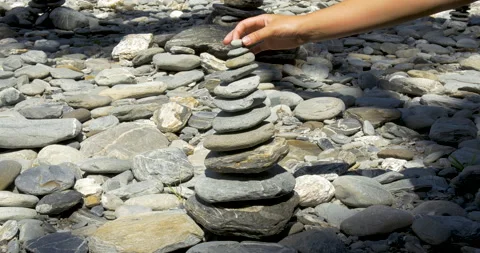 A woman completes a stone stack Stock Footage 148136377