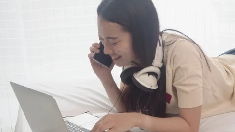 Woman with computer in the bed doing work on laptop and talking with smartphone Stock Footage 108497463