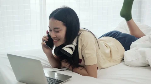 Woman with computer in the bed doing work on laptop and talking with smartphone Stock Footage 108497508