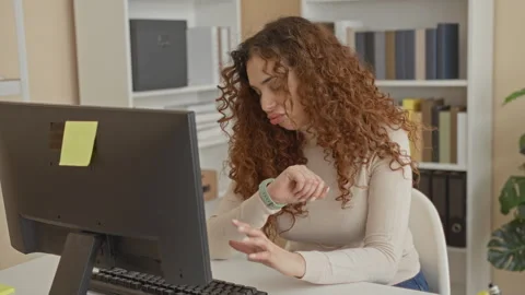 Woman at computer checks smartwatch, rests chin on hands and glances at mon.. Stock Footage 339257635
