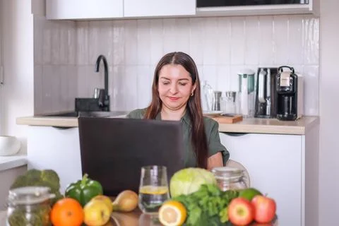 Woman at computer in kitchen creating menu using fresh vegetables and fruits Stock Photos