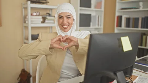 Woman at computer smiling forms heart shape with hands while seated at desk.. Stock Footage 347719703