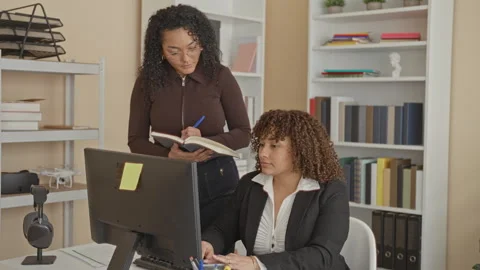 Woman at computer typing while colleague writes in notebook in a building; .. Stock Footage 337394548