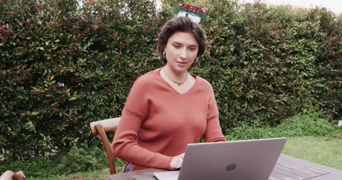 Woman concentrating on open laptop on table at patio typing then shifting to Stock Footage 335683036
