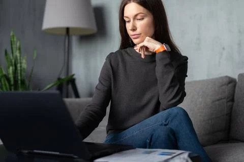Woman concentrating while using a laptop computer at home, sitting comfortably o Stock Photos