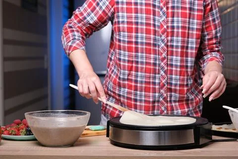 Woman cooking delicious crepe on electric pancake maker in kitchen, closeup Stock Photos