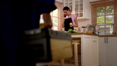 Woman cooking in kitchen while talking on mobile phone as technician 動画素材 340151975