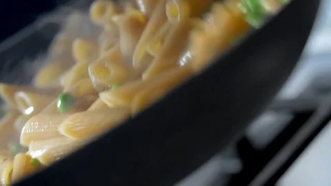 A woman is cooking penne pasta in a skillet Stock Footage