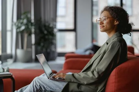 Woman on couch using laptop computer in comfort near window with houseplant in Stock Photos