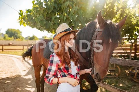 Woman cowgirl standing and taking care of horse in village Stock Photos
