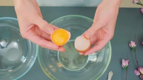 Woman cracking and separating eggs over glass bowls in kitchen Vidéo 342873378