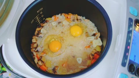 Woman cracking eggs and stirring rice with vegetables in kitchen 库存影片 342860281