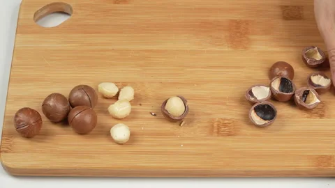 Woman Cracking Multiple Macadamia Nuts on Wooden Board. Stock Footage 332836644