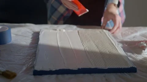 Woman creating textured pattern on canvas using plastic scraper on work table Stock Footage 327159061