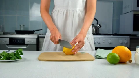 Woman cutting lemon into slices using sharp knife on wooden kitchen board. Vídeo Stock 313126637