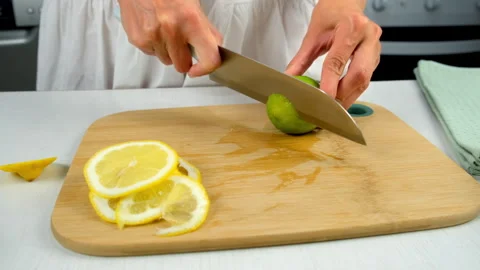 Woman cutting lime into slices using sharp knife on wooden kitchen board. Stock Footage 313115253