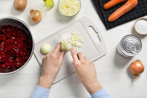 Woman cutting onion at white wooden table, top view. Cooking vinaigrette sala Stock Photos