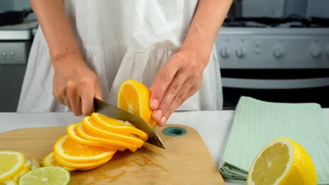 Woman cutting orange into slices using sharp knife on wooden kitchen board. Stock Footage 313116170