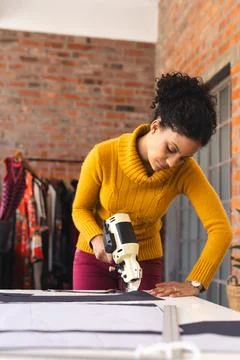 Woman cutting patterned fabric on worktable in sewing studio, with fabric cutter Stock Photos