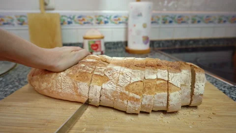 A woman is cutting a rustic bread over a wooden board with a large knife Stock Footage 163602861