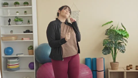 Woman dancing with hands raised, smiling, by an exercise ball and yoga mat .. Stock Footage 337373863