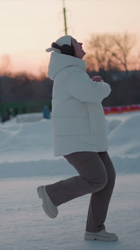 Woman Dancing Joyfully In Snow During Sunset With Headphones And White Winter Stock Footage 346774553