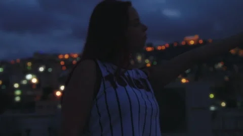 Woman dancing while in front of city lights at sunset Stock Footage 275099415