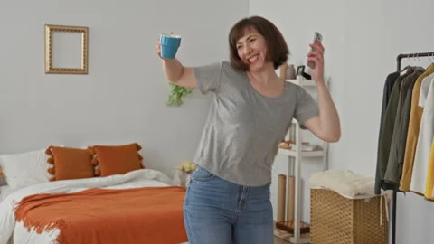 Woman dancing while holding a blue coffee mug and smartphone, arms raised a.. Stock Footage 339245038