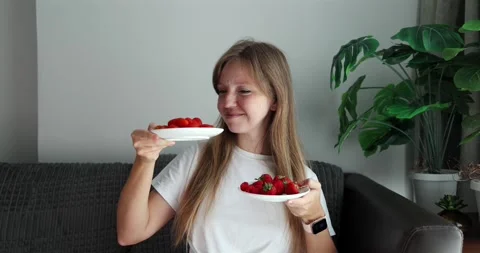 Woman deciding between cherry tomatoes and strawberries indoors, Видео 305931232