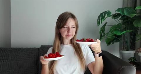 Woman deciding between tomatoes and strawberries, holding plates Vídeos de archivo 305932053