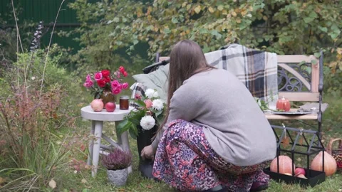 A woman decorates a bench and a table in the garden with flowers and pumpkins Stock Footage 161615697