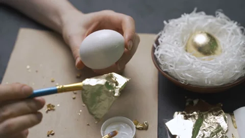 Woman decorates eggs for Easter using gold foil Stock Footage 101473648