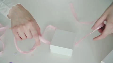 Woman decorates present box with light-pink ribbon bow 動画素材 168977424