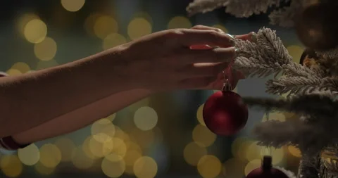 Woman decorating Christmas tree with red ball on a blurry bokeh background with Stock Footage 293609783