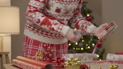 Woman decorating gift with ribbon at table with ornaments and wrapping supplies Stock Footage 342180732
